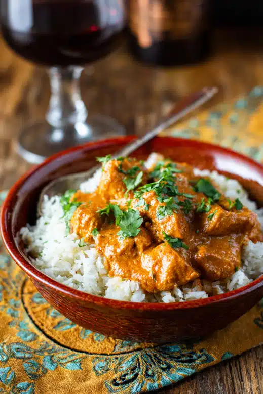 Close-up of slow cooker butter chicken in a red ceramic bowl served over basmati rice and garnished with cilantro


